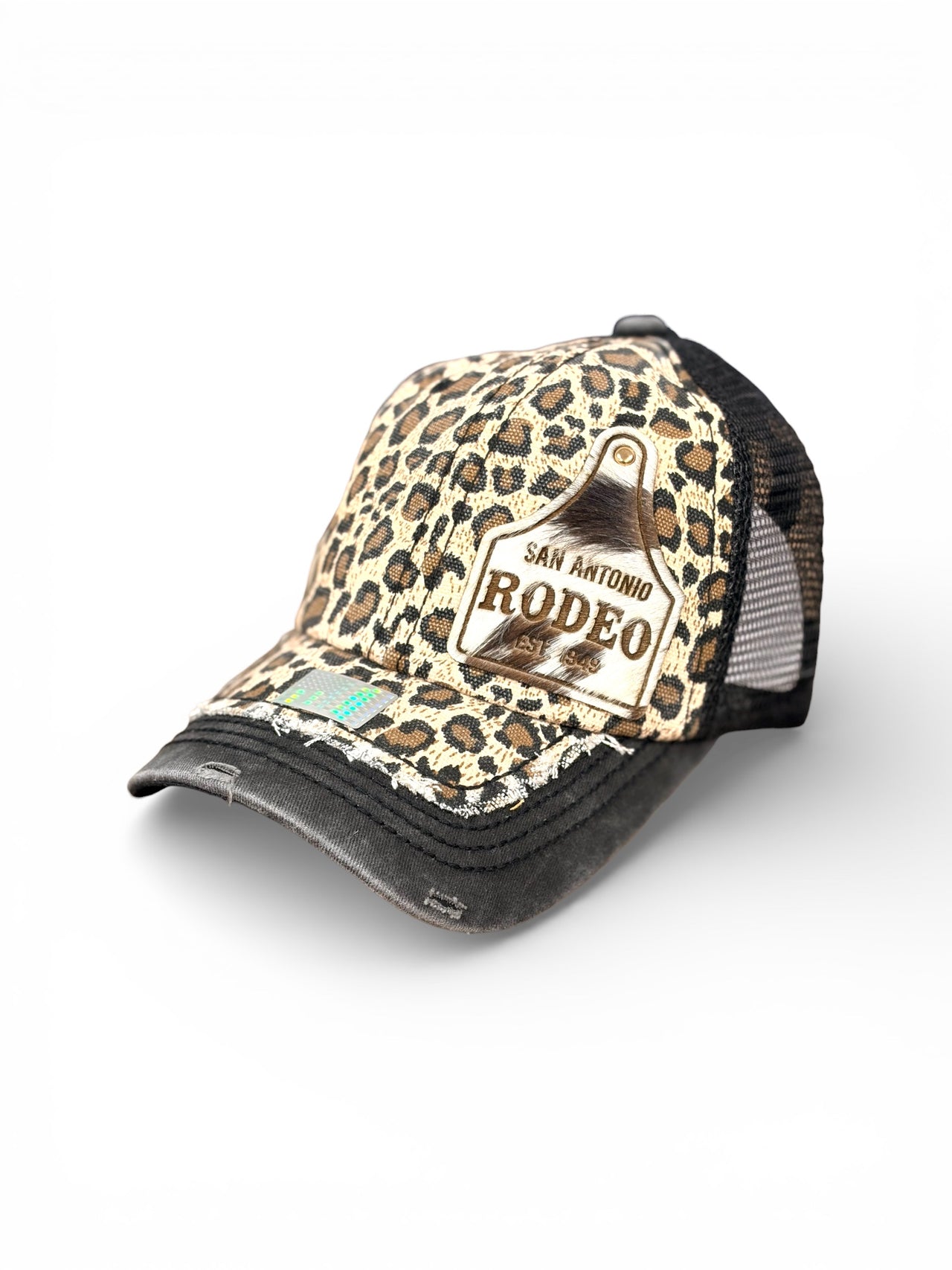 Leopard print trucker hat with genuine cowhide Rodeo San Antonio patch, distressed denim bill, and black mesh back.